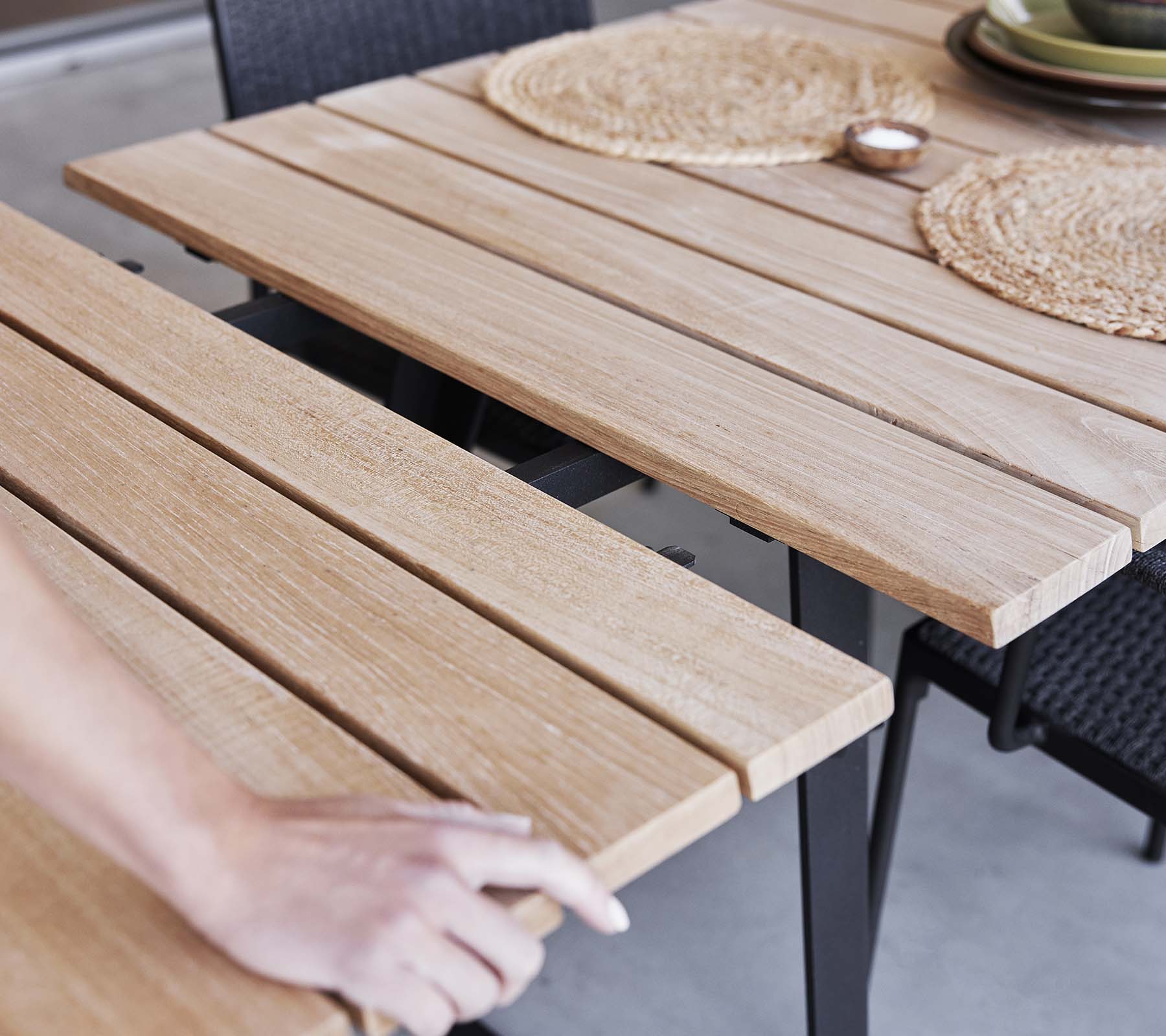 Detalje af et træbord med lameldesign, dækkeservietter og en minimalistisk æstetik, perfekt til spisning eller sammenkomster.