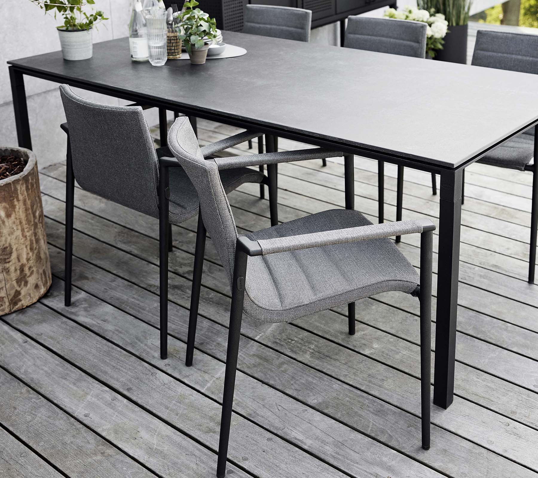 Stilfuld spiseopsætning med et strømlinet bord og moderne grå core-stole, omgivet af naturlige elementer og grønt.