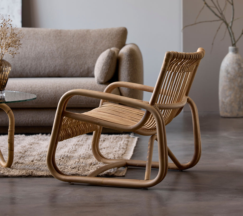 Rattan stol ved siden af en beige sofa og glasbord i et moderne loungeområde.