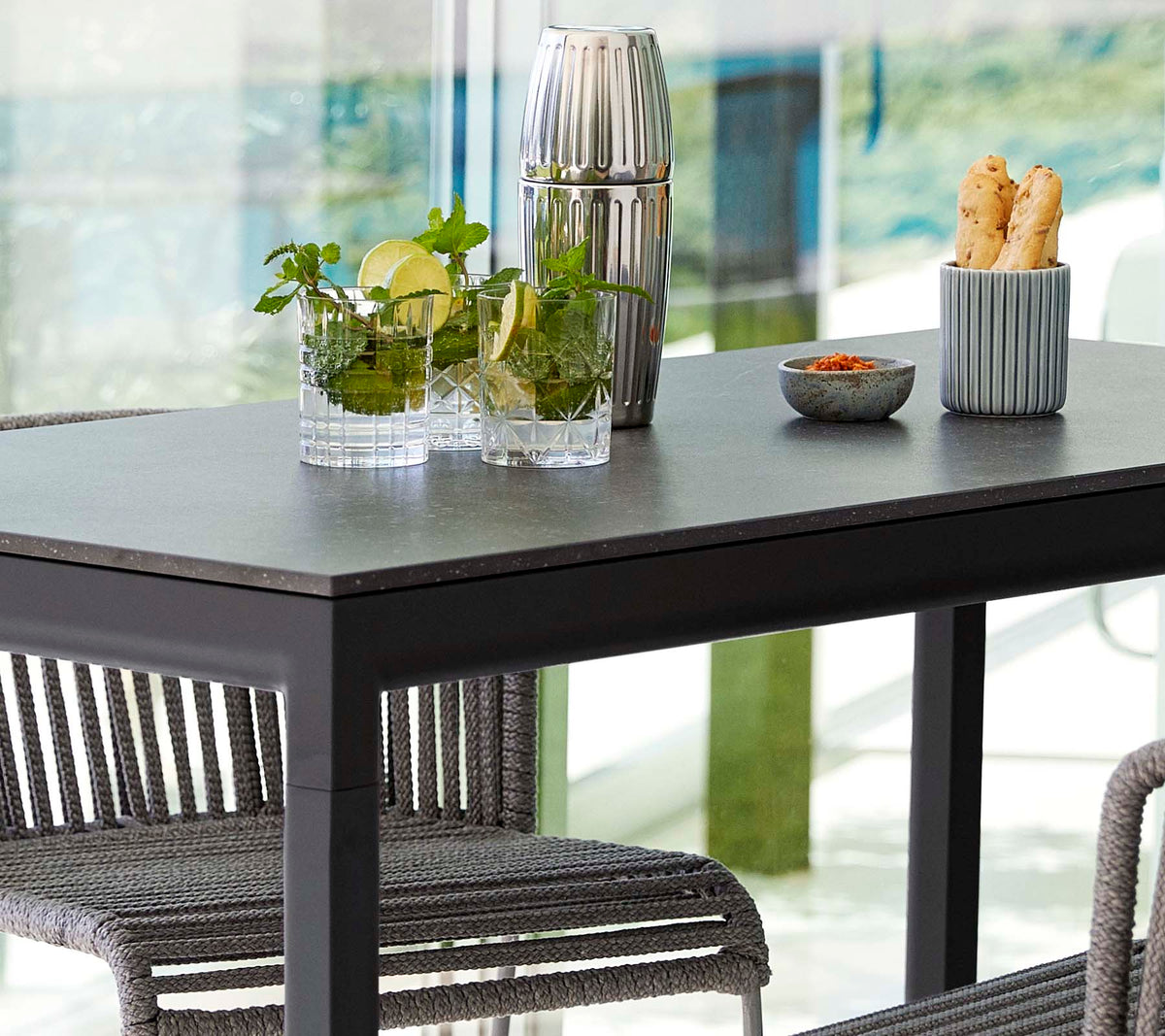 Et moderne bord sat med planter i glasvaser, en dekorativ beholder og en skål med snacks, omgivet af stilfulde stole.