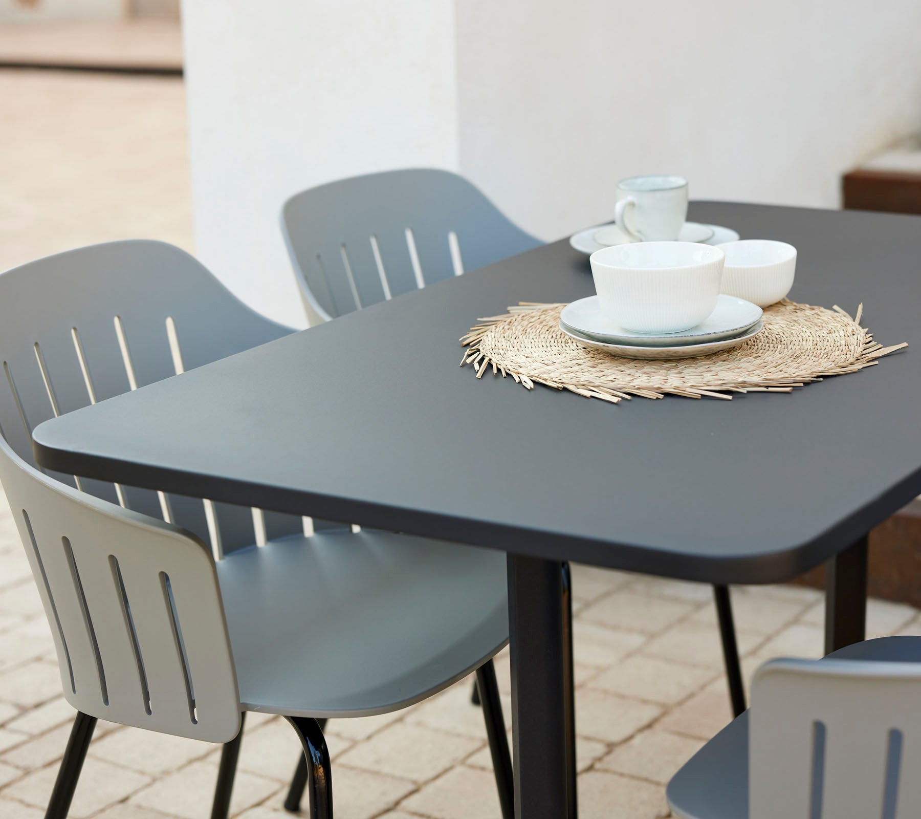 Moderne cafe borde sæt med en sort bordplade, omgivet af grå stole, med tallerkener og kopper på en stråunderlag.