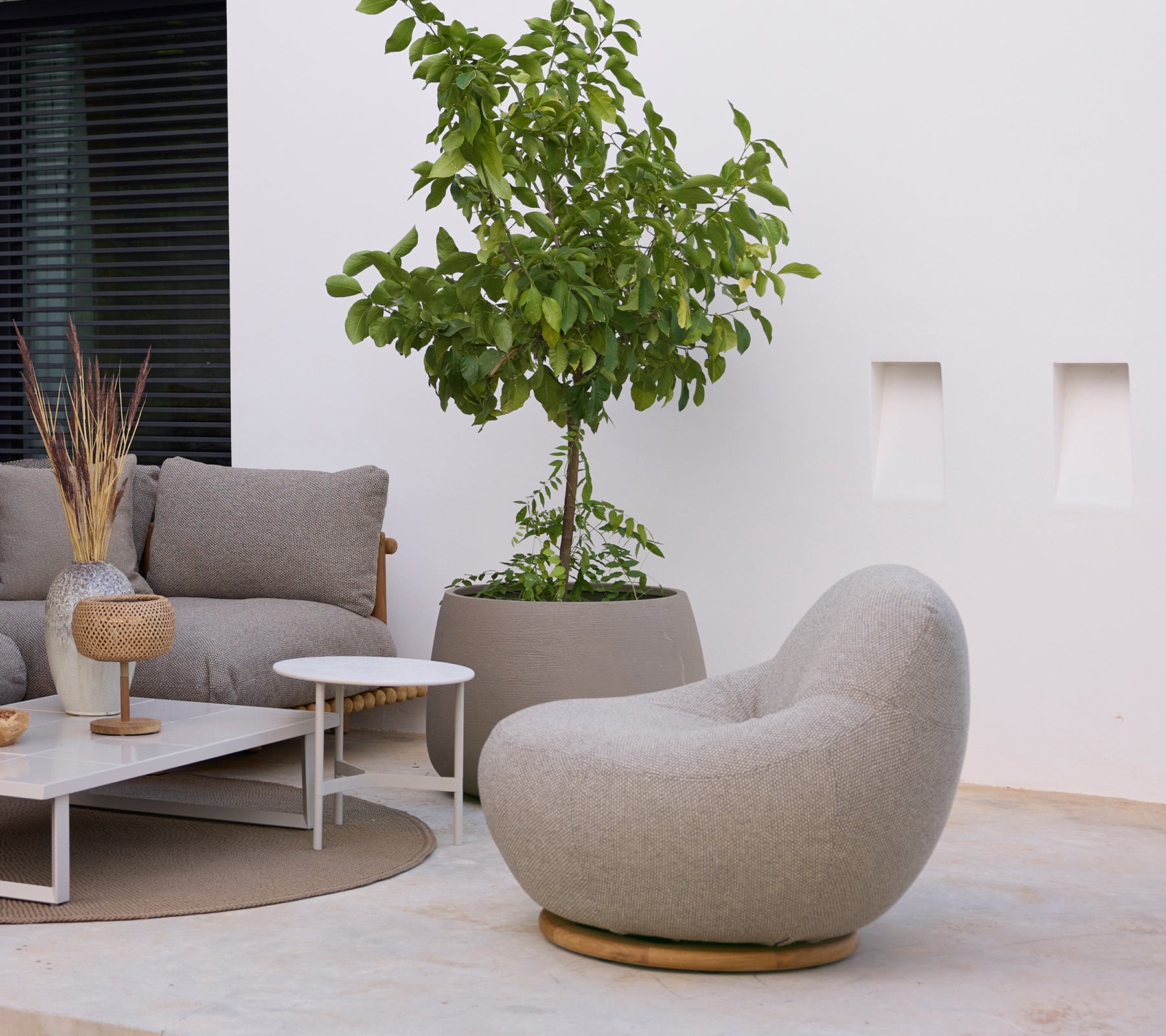 Moderne loungeområde med en grå stol, sofa, hvidt kaffebord og grøn plante.