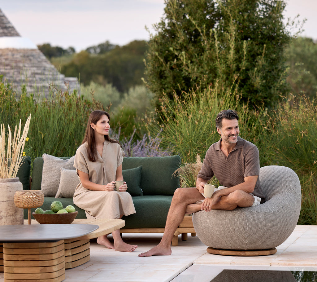 Moderne lounge med grøn sofa, grå rund stol og brun bord omgivet af planter.