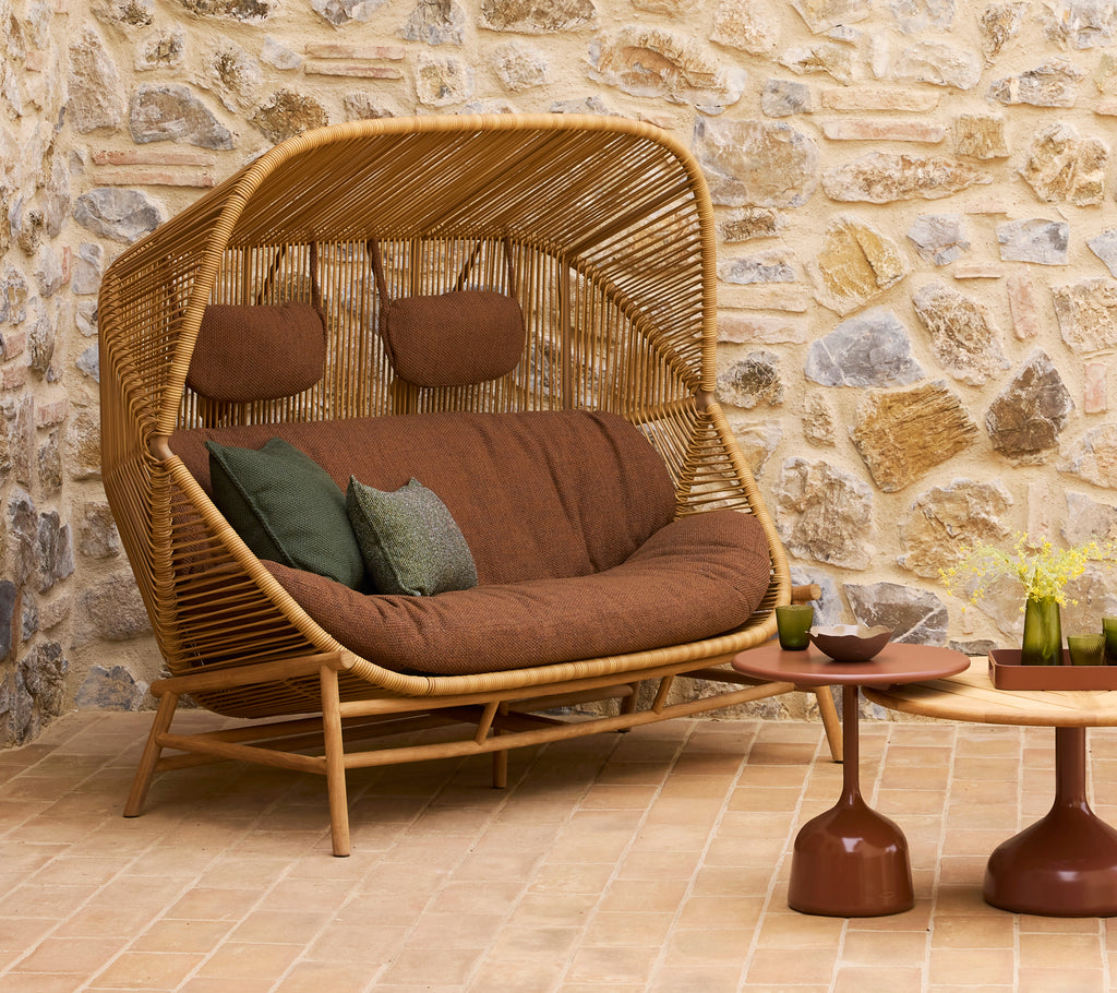 En stilfuld rattan-sofa med brune puder og grønne pyntepuder, ledsaget af to moderne sofaborde.