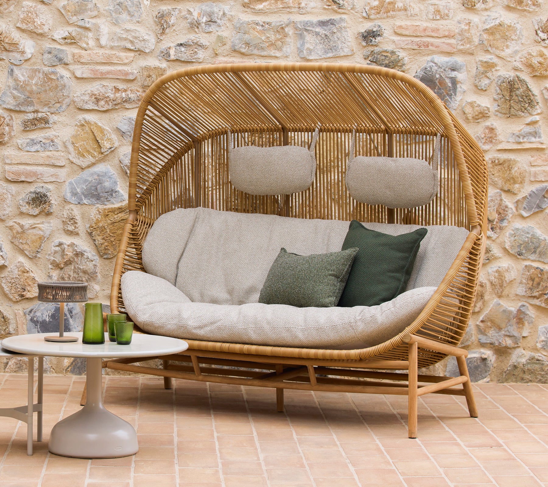 Hive sofa med bløde puder og grønne accenter sammen med Glaze kaffeborde, sat mod en naturlig stenbaggrund.