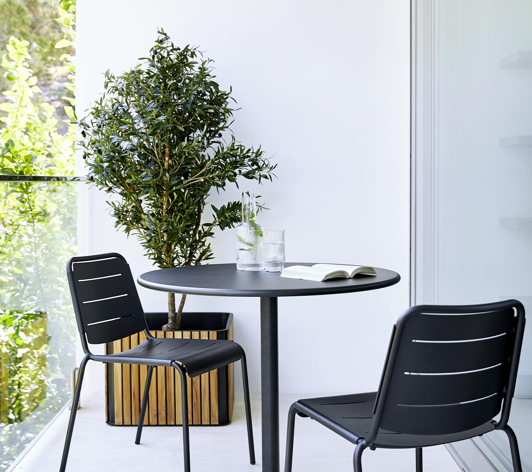 Et moderne spiseopsætning med et rundt bord, to sorte stole og en potteplante, der skaber en stilfuld og indbydende atmosfære.