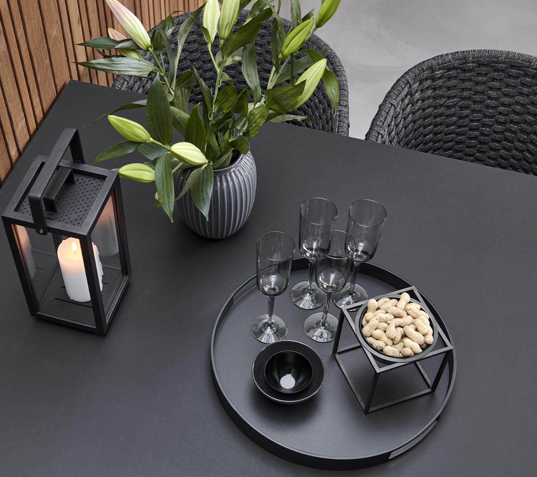 En stilfuld bordopdækning med en lysestage, en vase med blomster, glas og et serveringsfad med snacks.