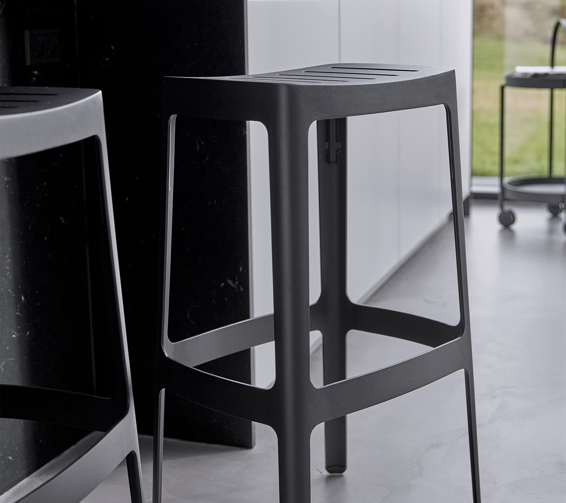 En slank, moderne barstol med et minimalistisk design, der har en robust struktur og en elegant sort finish.