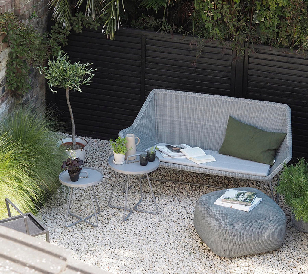 Moderne grå sofa med grøn pude og grå sidebord i et minimalistisk loungeområde.