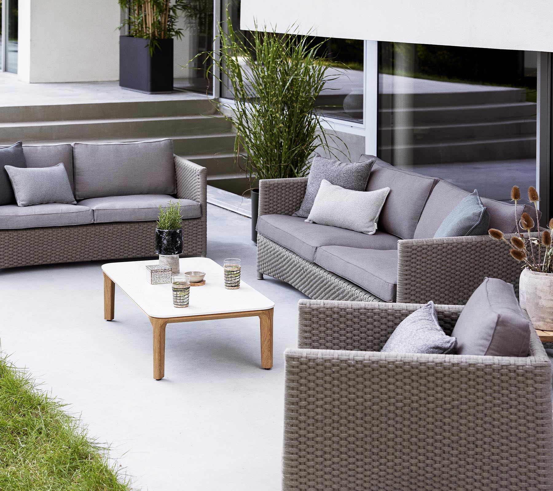 Moderne udendørs siddearrangement med en 2-personers sofa, 3-personers sofa, loungestole og et kaffebord med dekorationsgenstande.