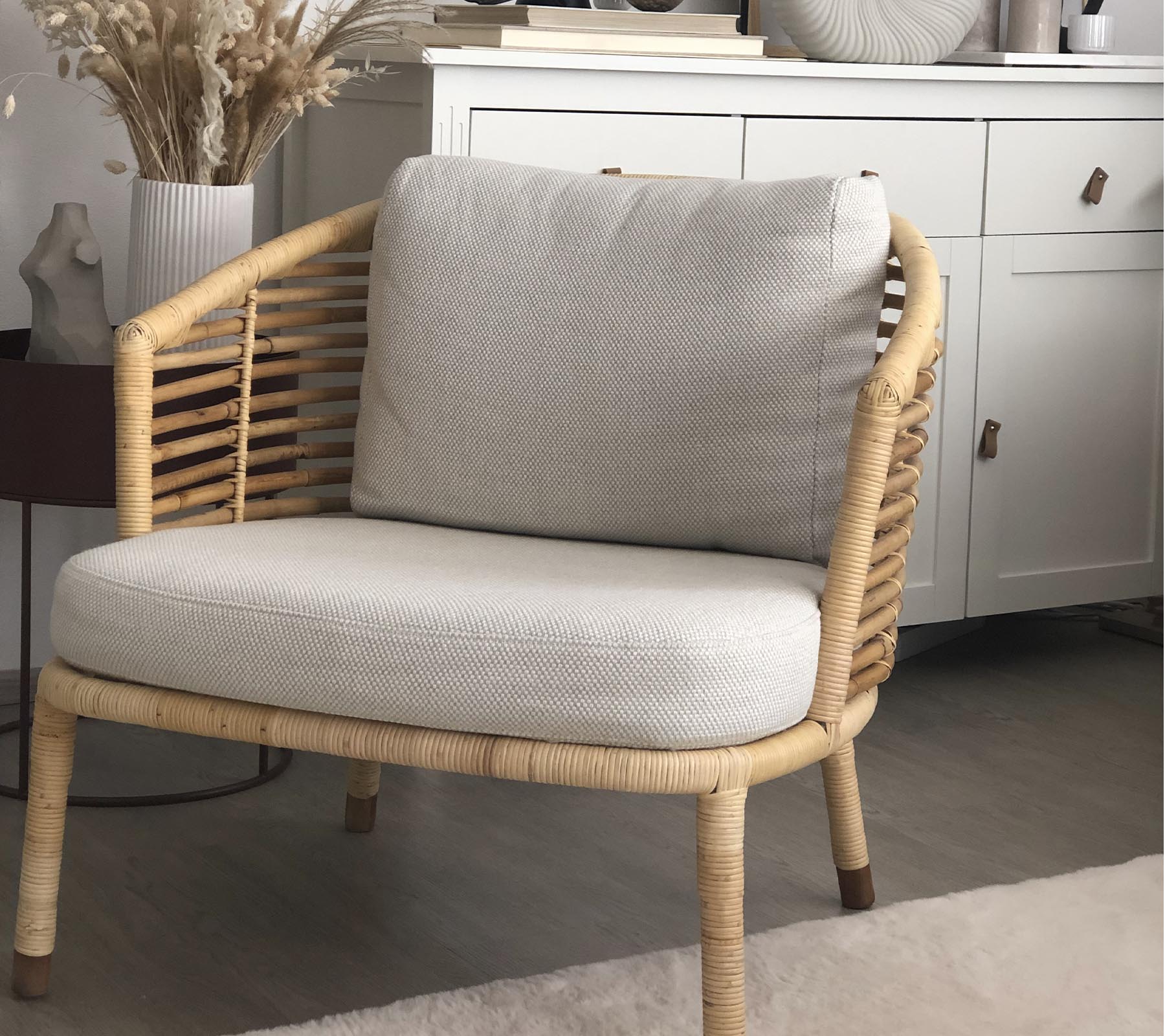 En stilfuld stol med et vævet design og bløde puder, parret med en dekorativ plante og en stilfuld opbevaringsenhed i baggrunden.