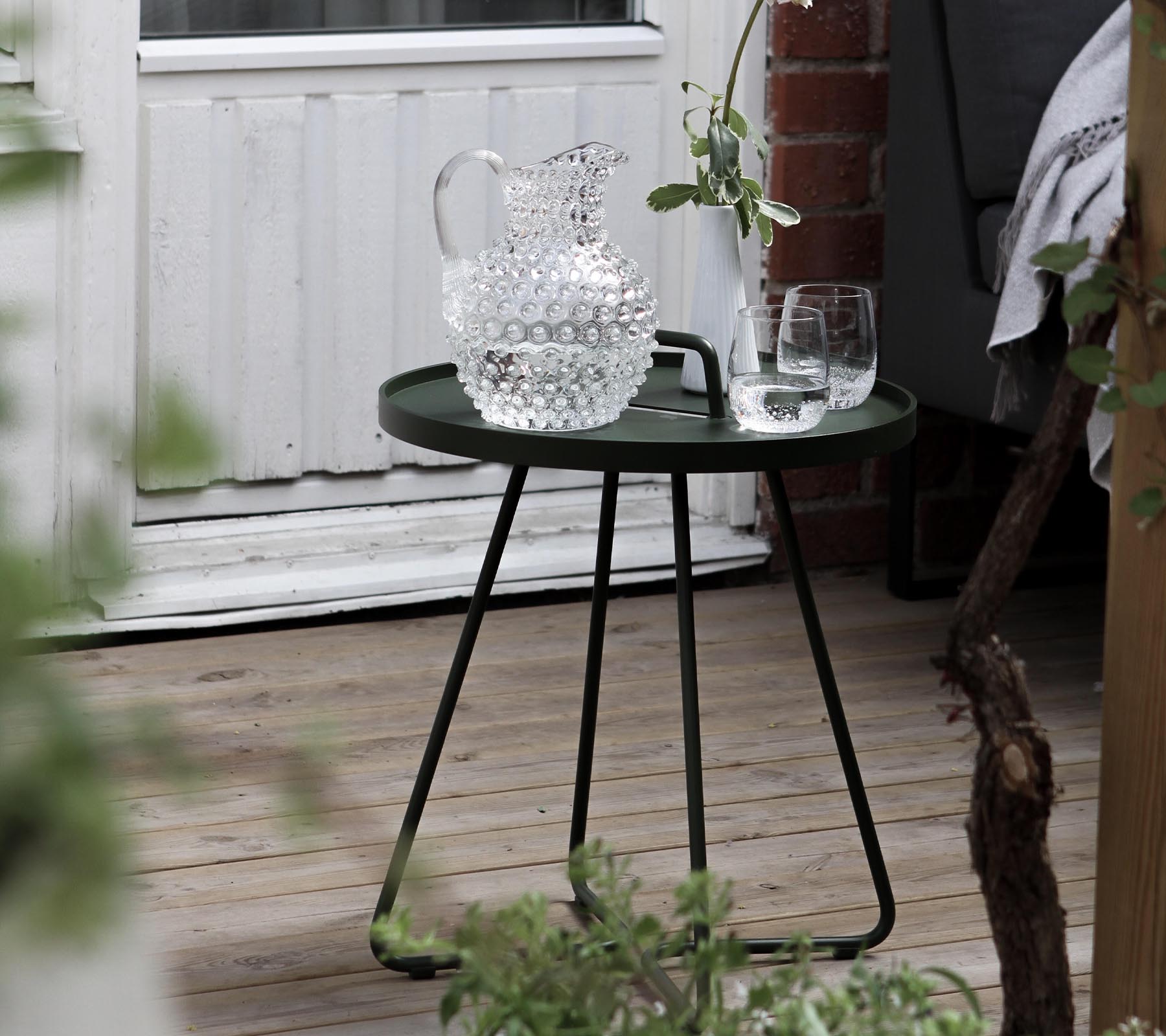 Et stilfuldt grønt sidebord med en krystalkaraffel og to glas, suppleret af frisk grønne planter i området.