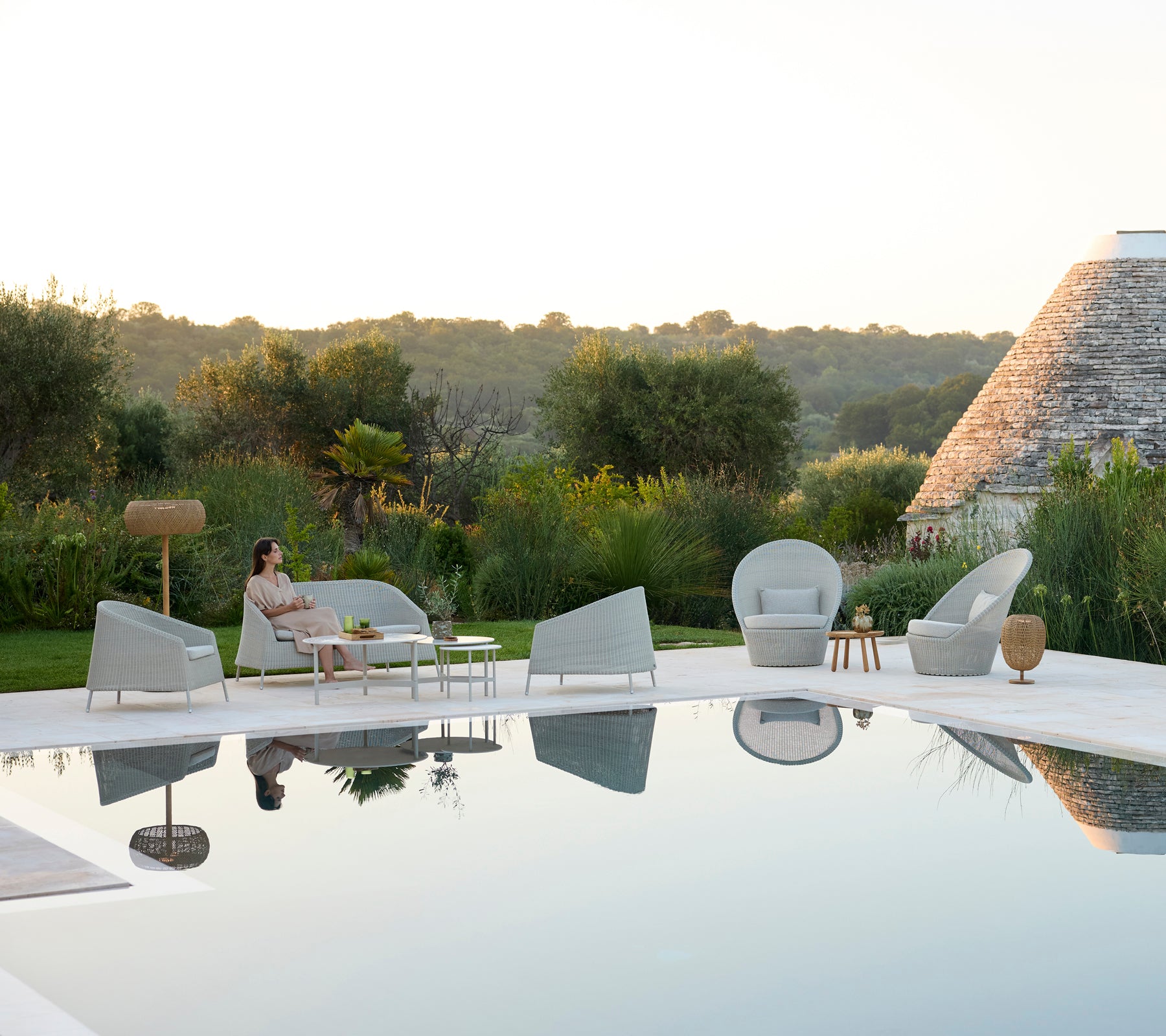 Moderne udendørs loungeområde med grå stole og et hvidt bord ved en pool.