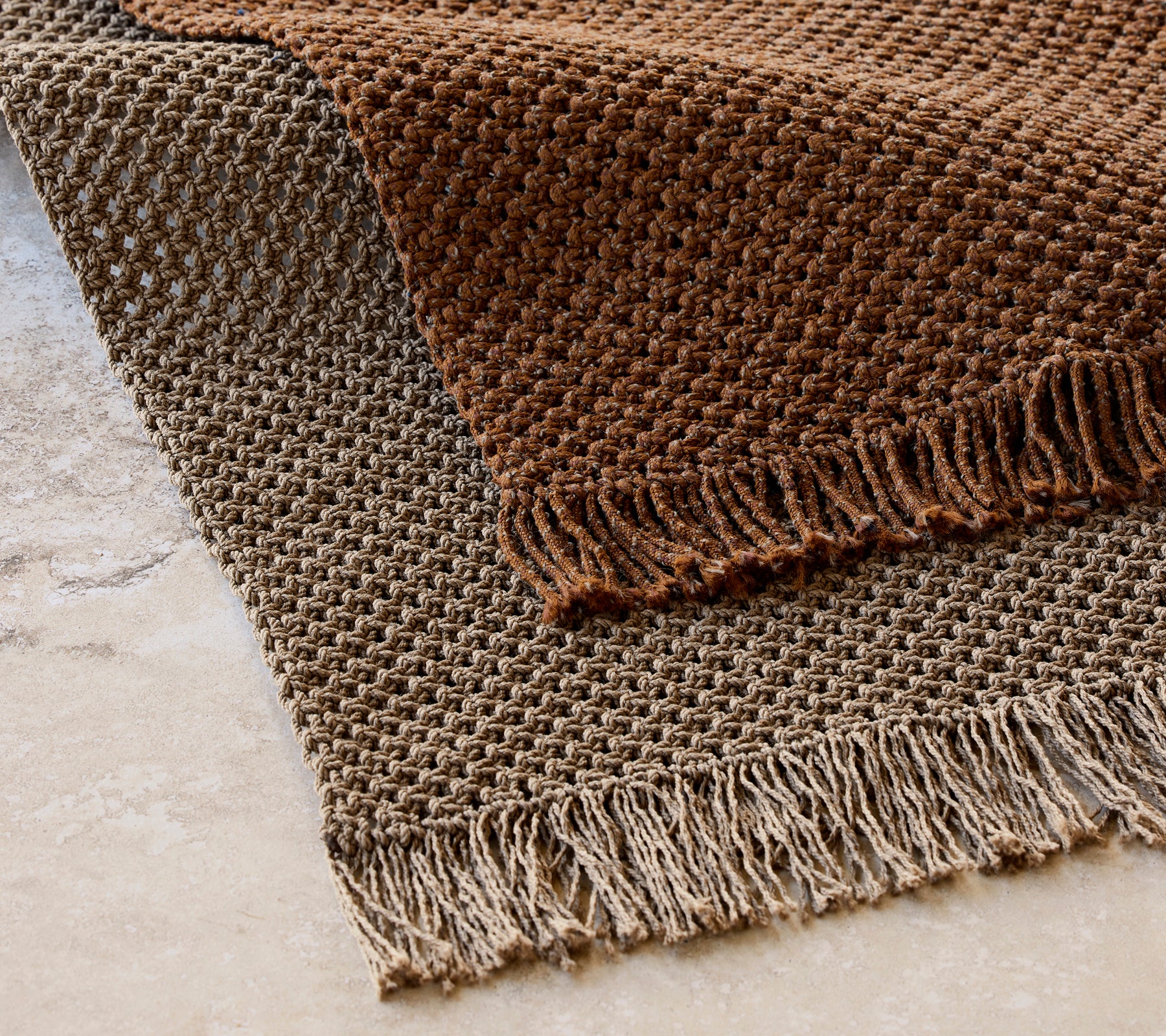 Strikket tæppe måler 240x170 cm i et struktureret mønster med frynser, med varme brune toner.