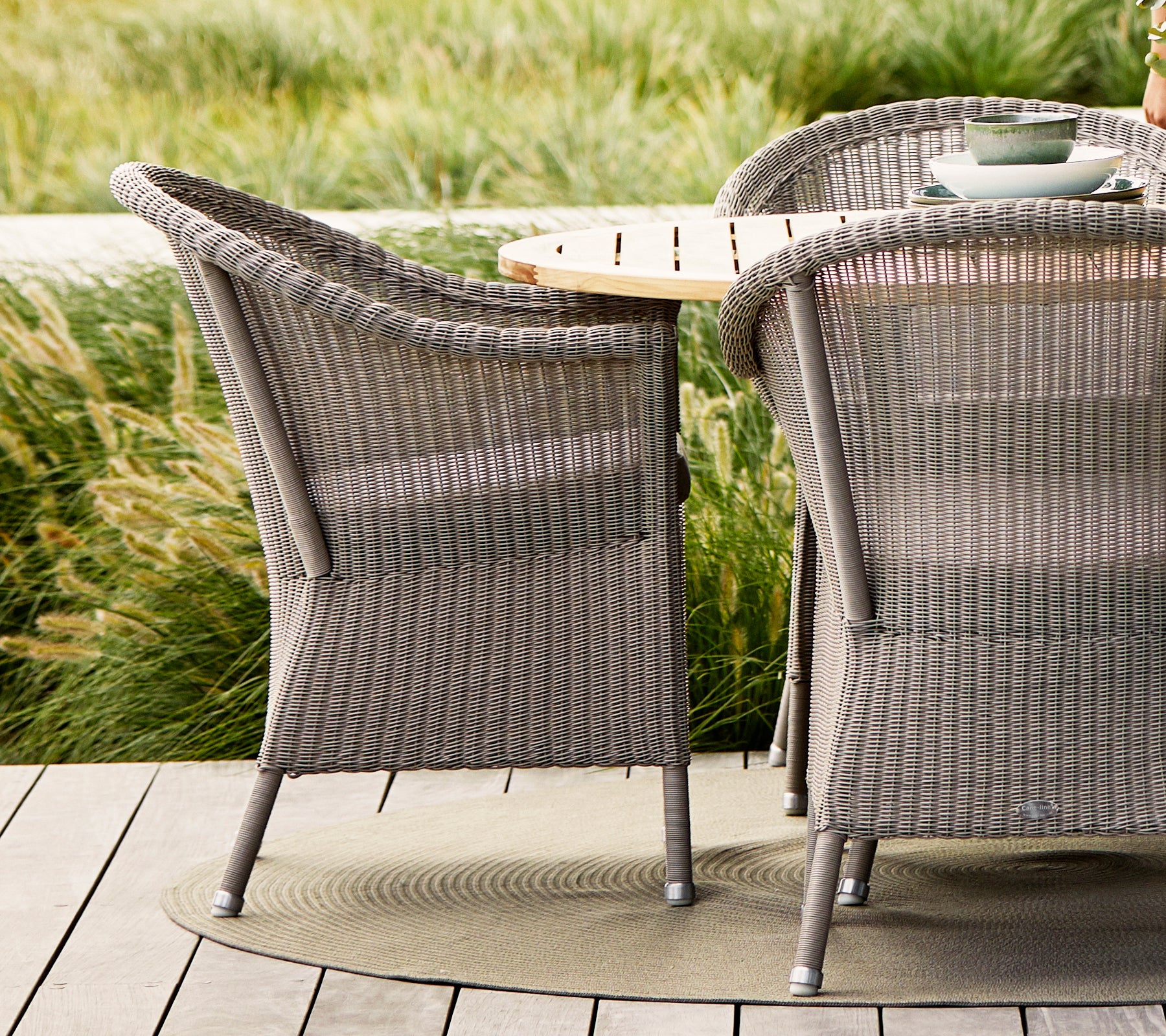 Taupe Lansing stole med struktureret vævet design, parret med et bord af naturligt træ og omkranset af frodige planter.