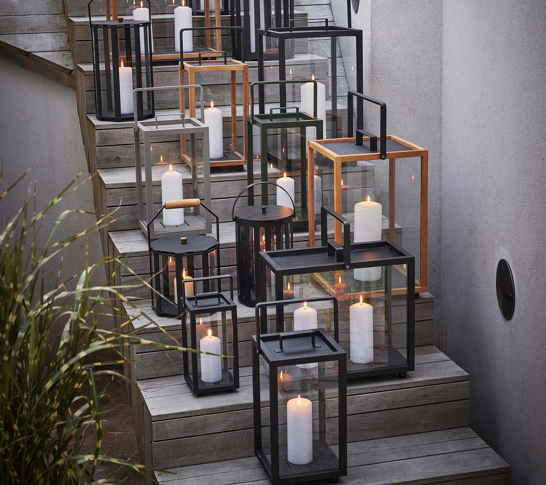 En samling af forskellige lanterner med stearinlys arrangeret på en trappe, der viser en blanding af sorte og metalliske rammer.