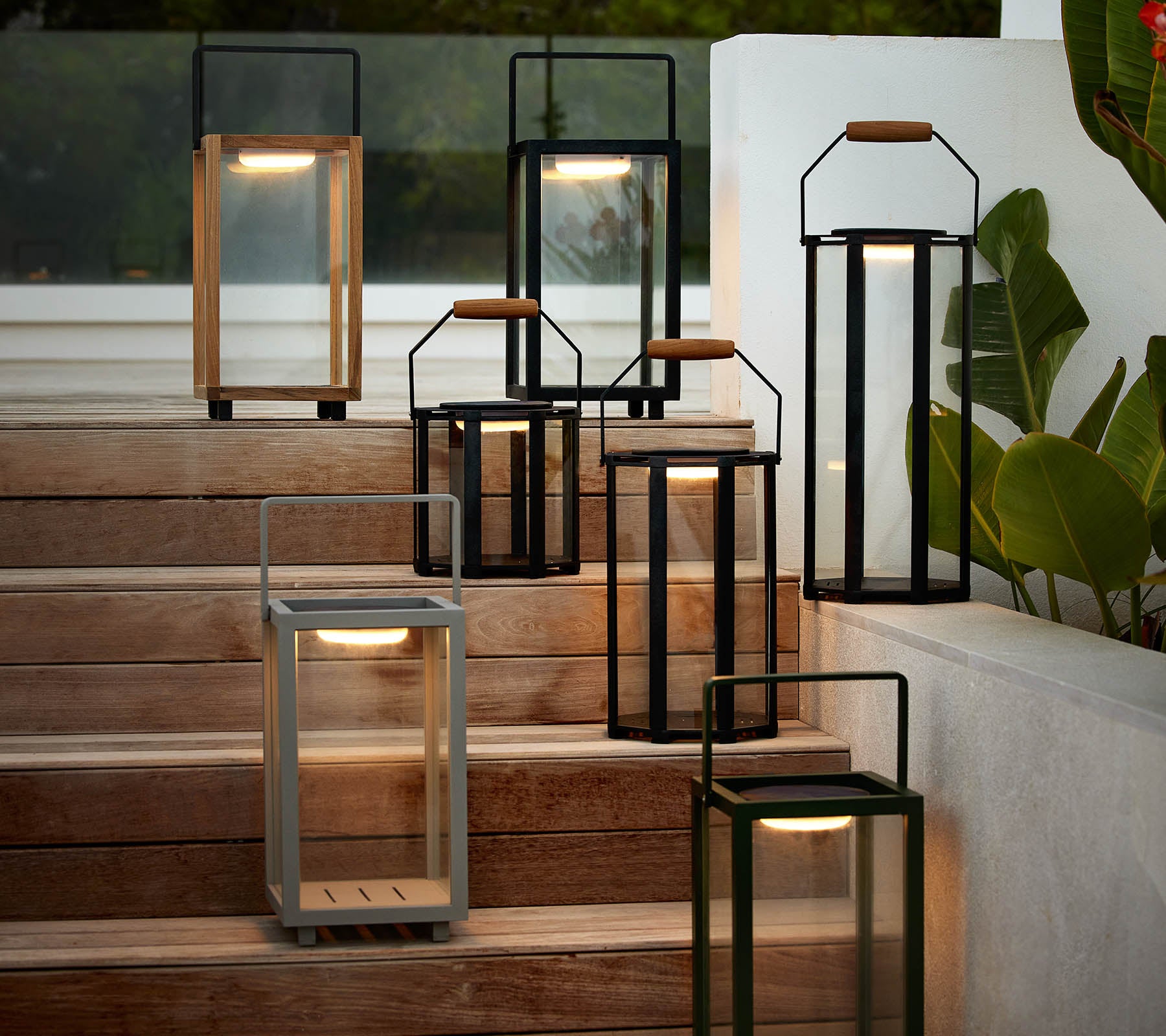 En samling af moderne lanterner i forskellige stilarter og farver, arrangeret på en trappe, der fremhæver deres elegante design og varme belysning.