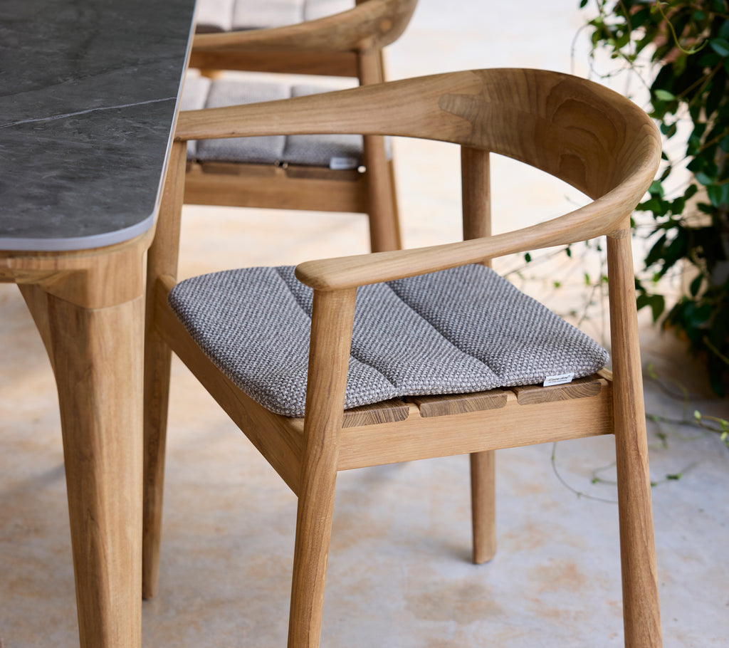 Moderne træstol med grå pude ved siden af et bord i en loungeindstilling.