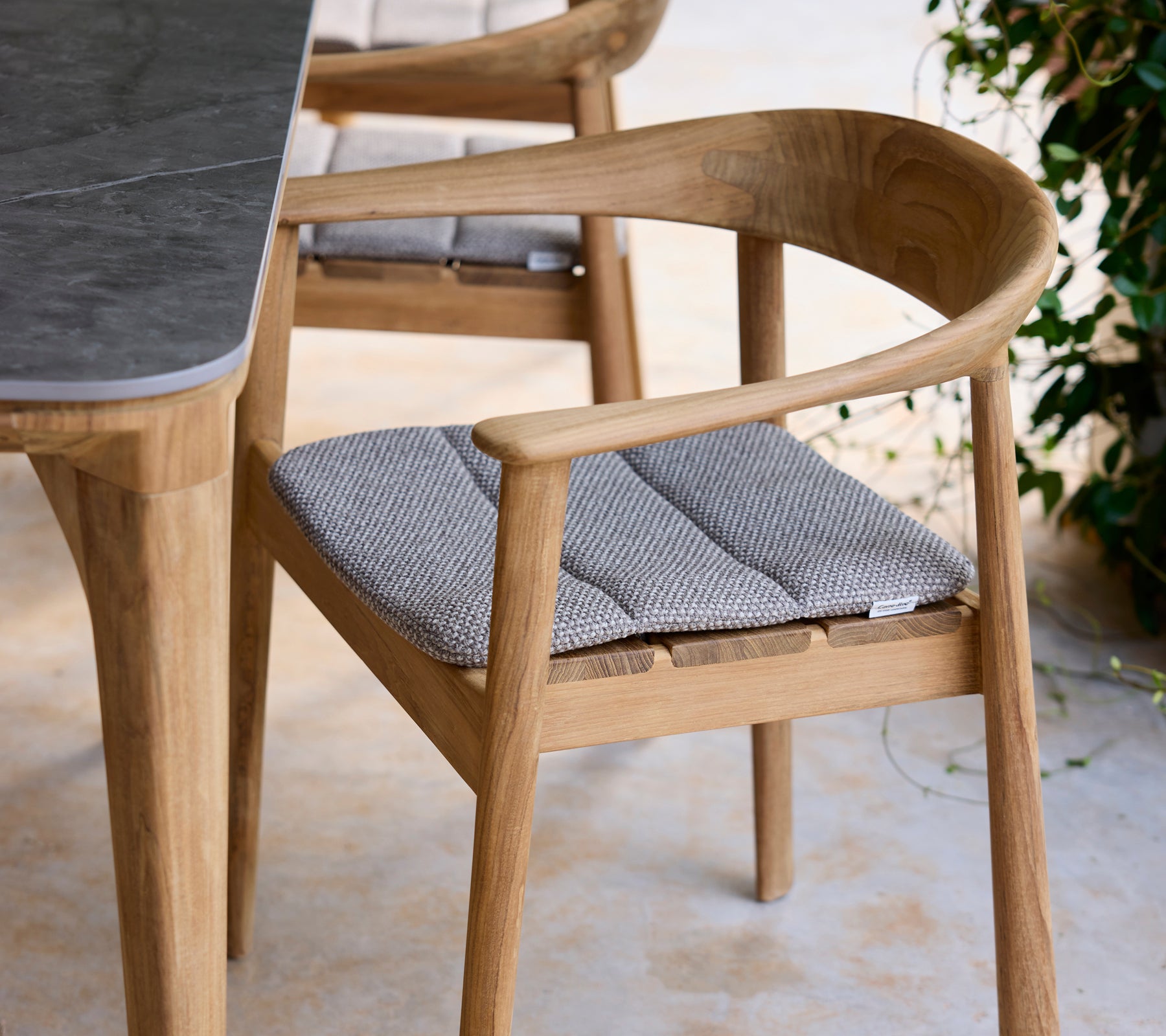 Moderne træstol med grå pude ved siden af et bord i en loungeindstilling.