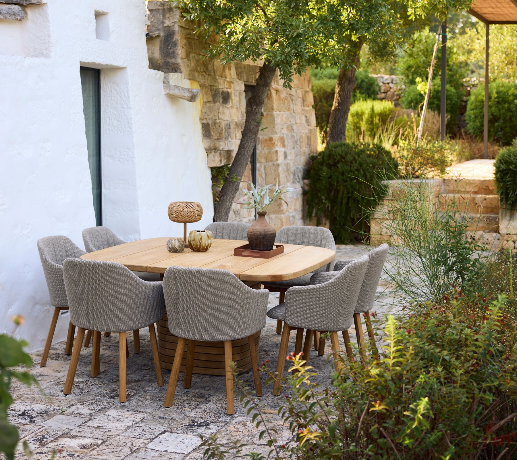 Moderne træ spisebord omkranset af grå stole i en haveindstilling.