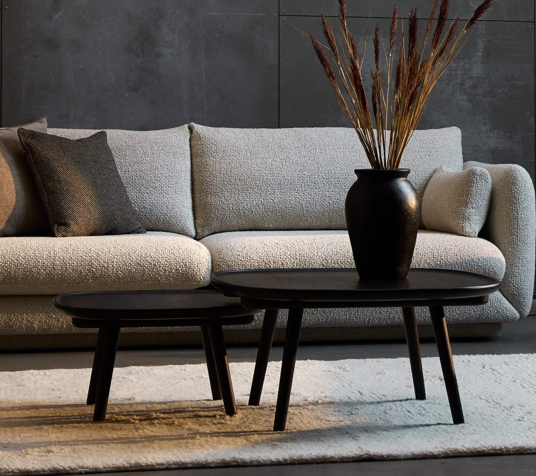 To elegante sorte kaffeborde i forskellige størrelser, suppleret af en dekorativ vase med tørrede planter, sat mod en hyggelig sofa.