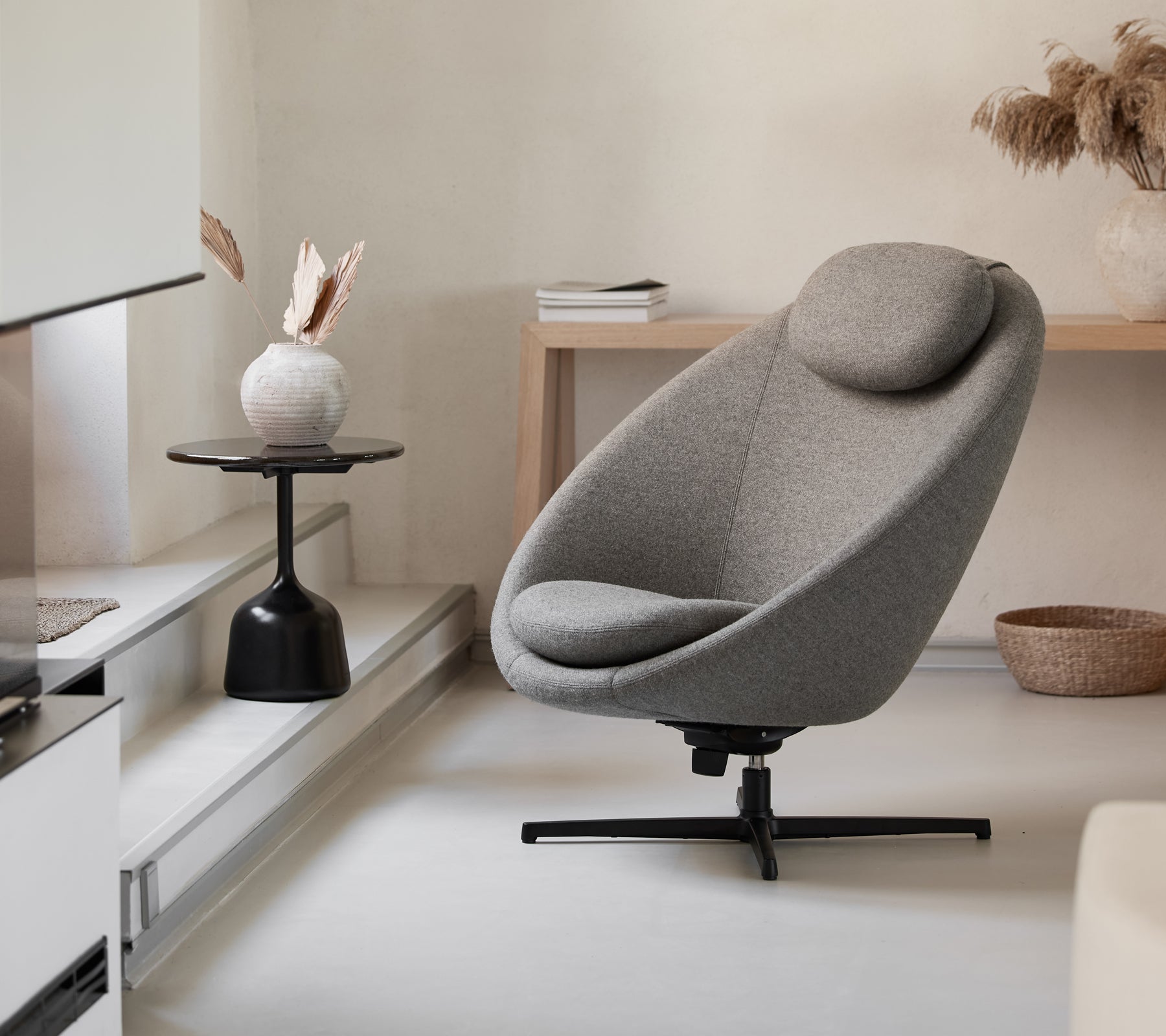 Stilfuld grå stol med en buet form og støttende nakkestøtte, suppleret af et minimalistisk sidebord og dekorative elementer.