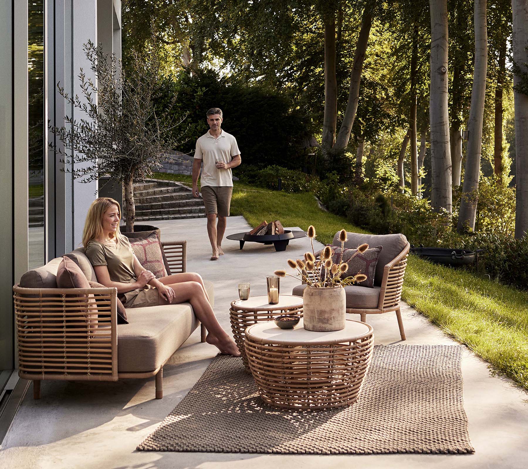 Et hyggeligt siddearrangement med en Sense-sofa og lounge stol, ledsaget af et kurvkaffebord og dekorative elementer.