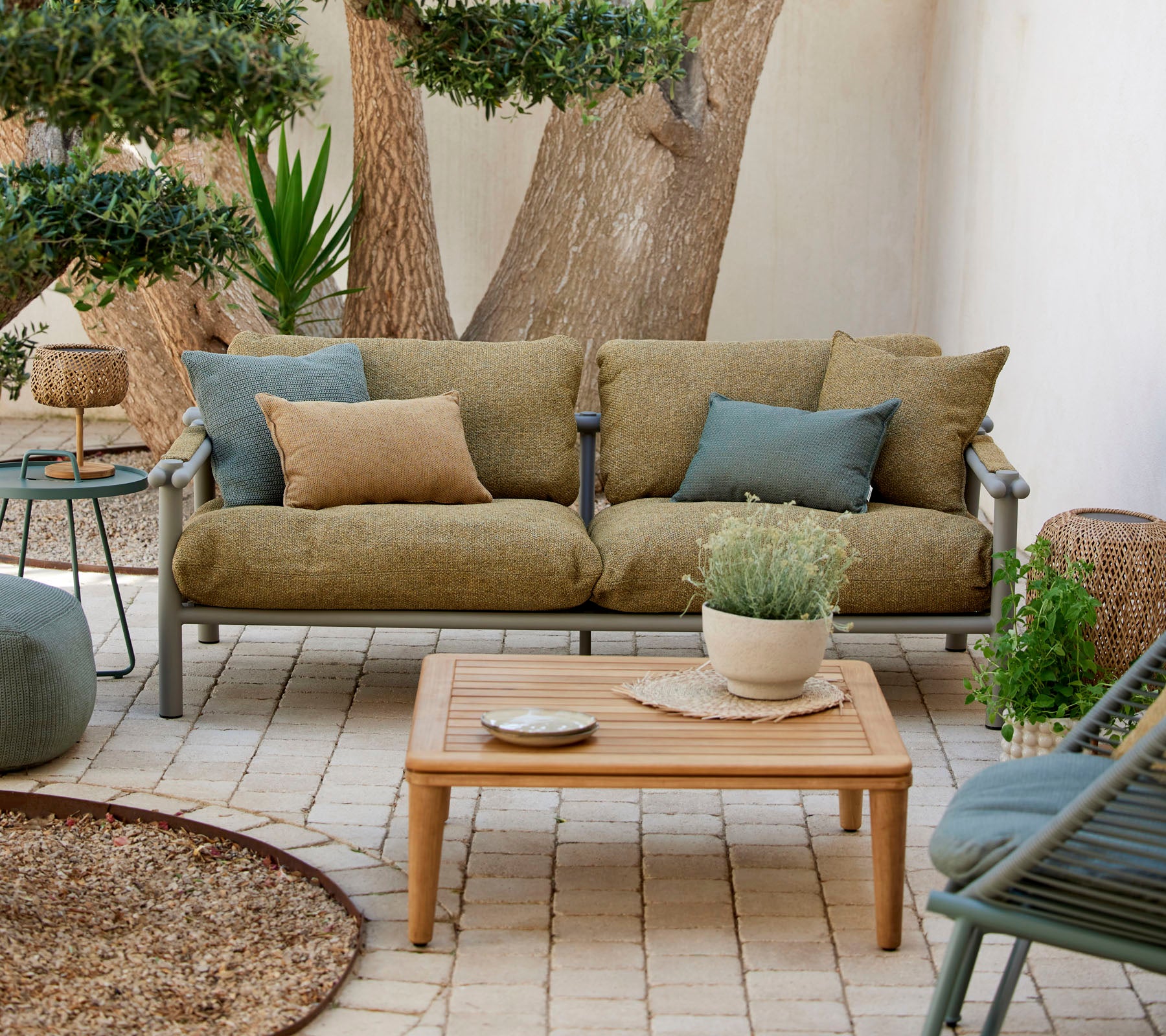 Comfortabel siddeområde med en grøn sofa med puder, et trækaffebord og dekorative planter i en rolig indstilling.