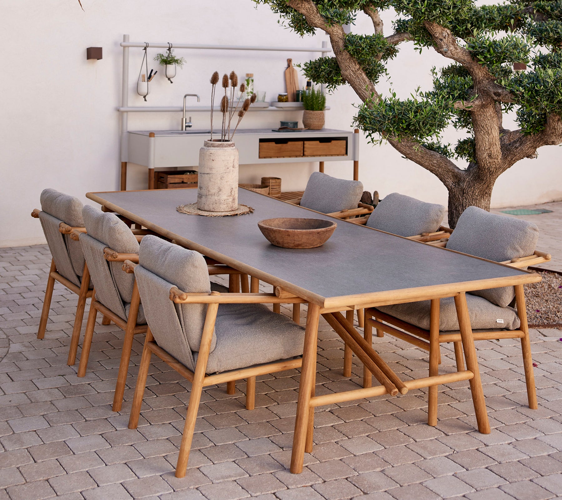 Teak spisebord omkranset af komfortable stole med naturlige elementer og en minimalistisk indretningsstil.