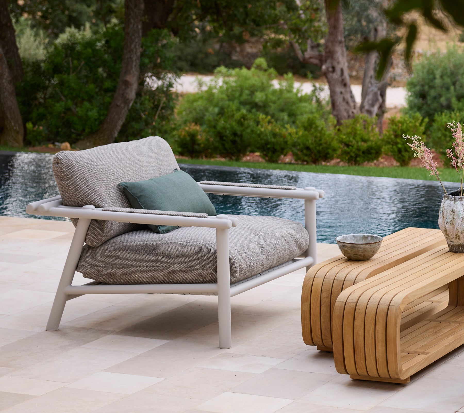 Moderne udendørs miljø med en grå sofa, grøn pude og et trækaffebord ved en pool.