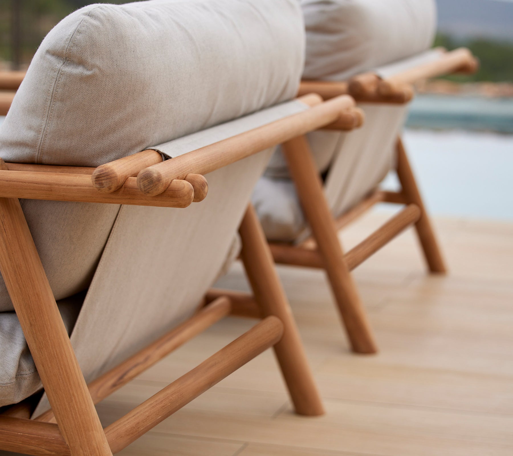 To stilfulde loungestole med teaktrærammer og komfortable beige puder, der viser et unikt stiksdesign på ryggen.