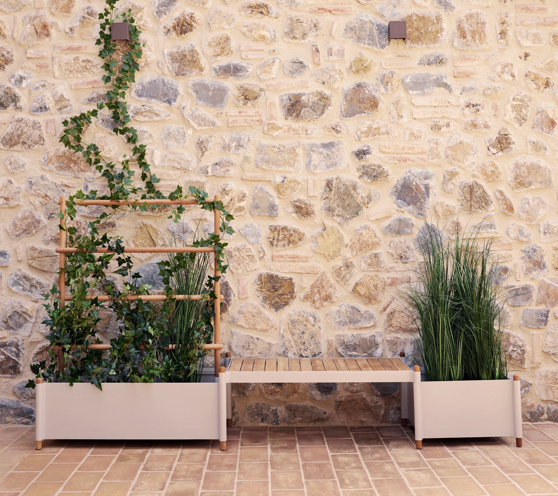 Sticks plantebænk med grønne planter mod en stenmur, der har en vertikal planteholder og to store plantekasser.