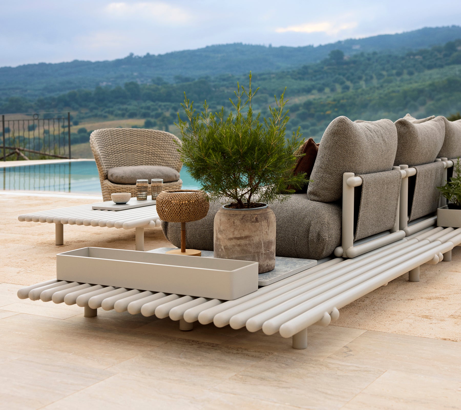 Et stilfuldt loungeområde med en komfortabel stol, en opbevaringsboks og en elegant platform af aluminium, omgivet af grønne planter.