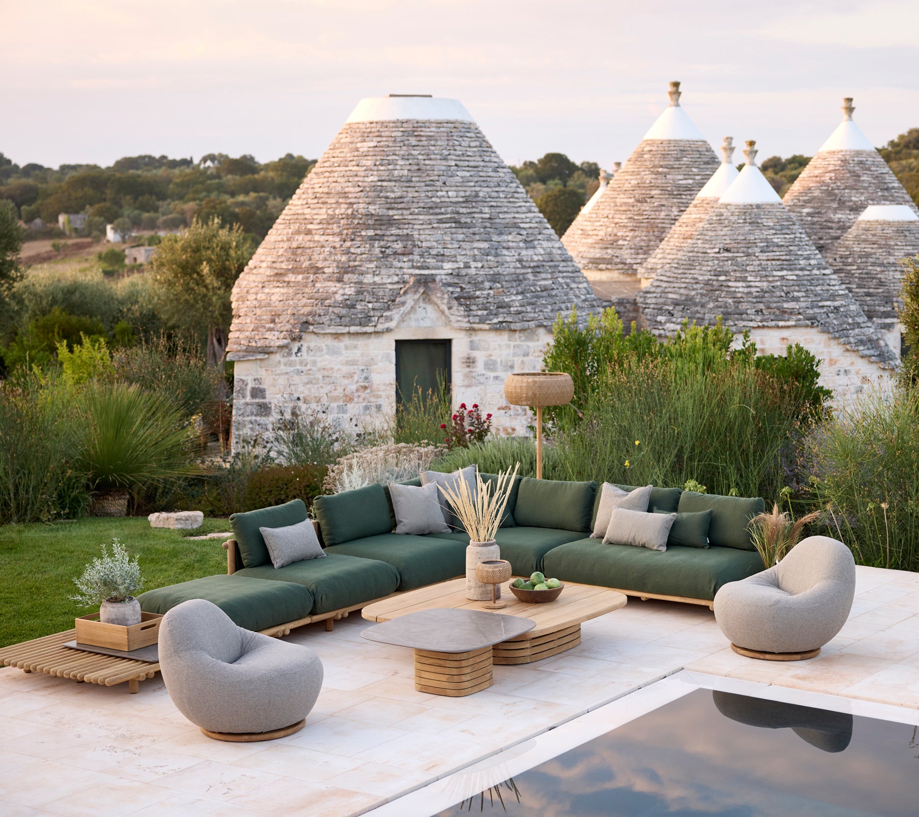 Moderne udendørs loungeområde med grøn sectional sofa, grå lænestole og trækaffebord.