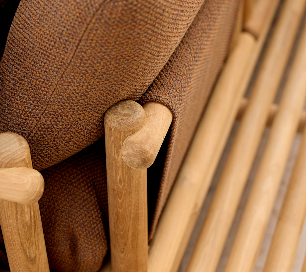 Teak loungestol med bløde puder og stilfulde træsider, der danner armlæn og grundstruktur.