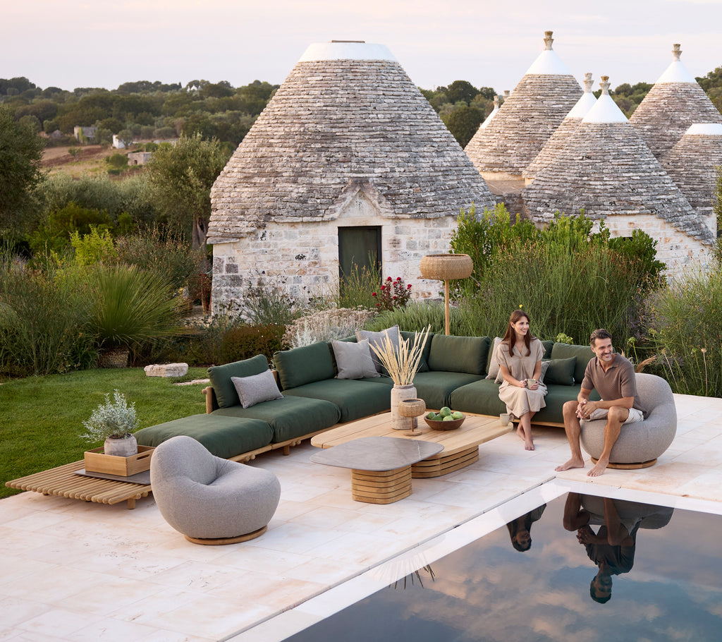 Modern udendørs loungeområde med en grøn sofa, grå stol og rundt sofabord.