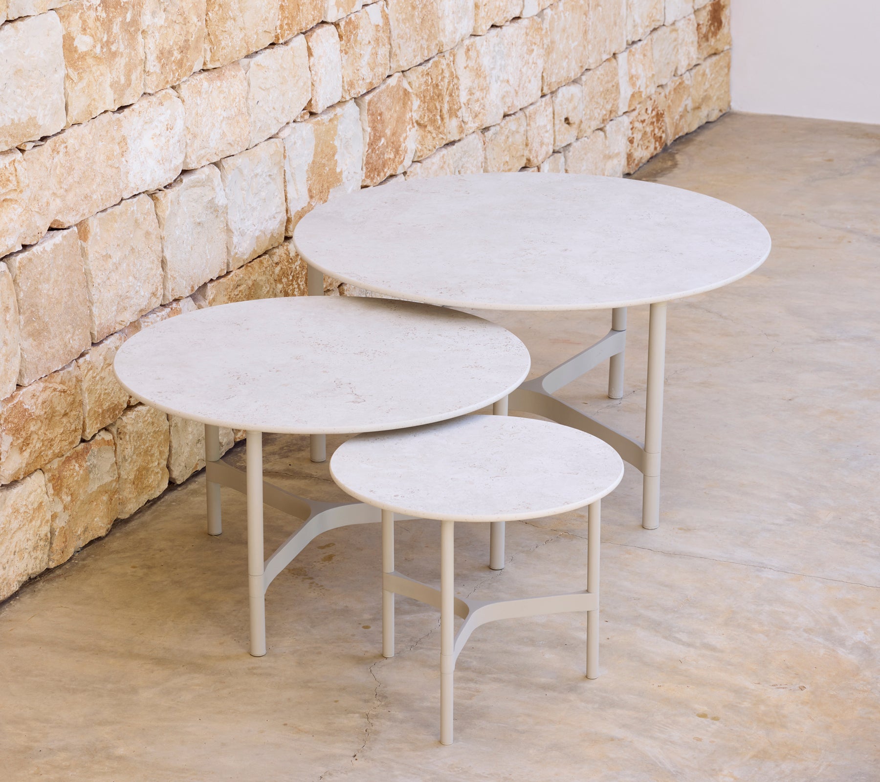 Tre moderne runde borde i forskellige størrelser mod en stenvæg.