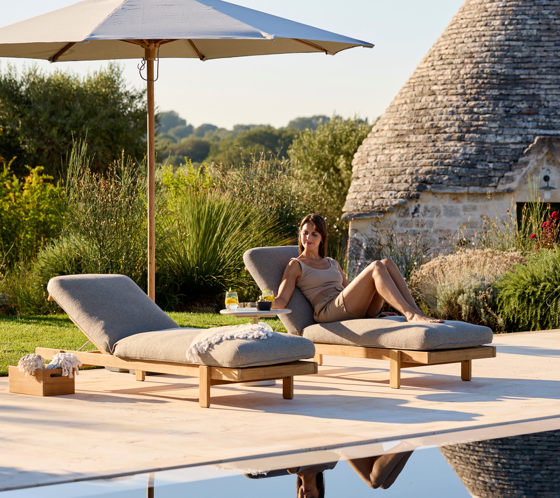 To liggestole med beige puder under en parasol i en fredfyldt udendørs omgivelser.