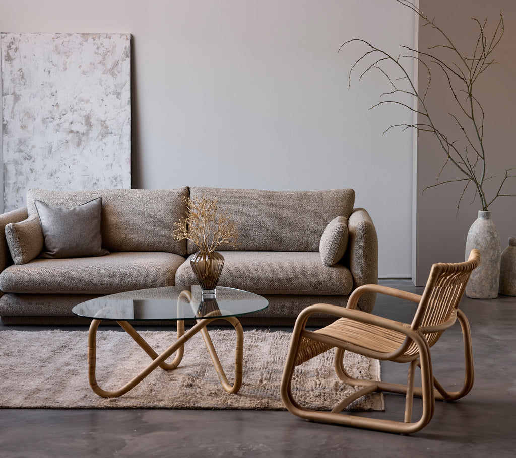 Moderne stueindretning med en beige sofa, glasbord og vævet stol.