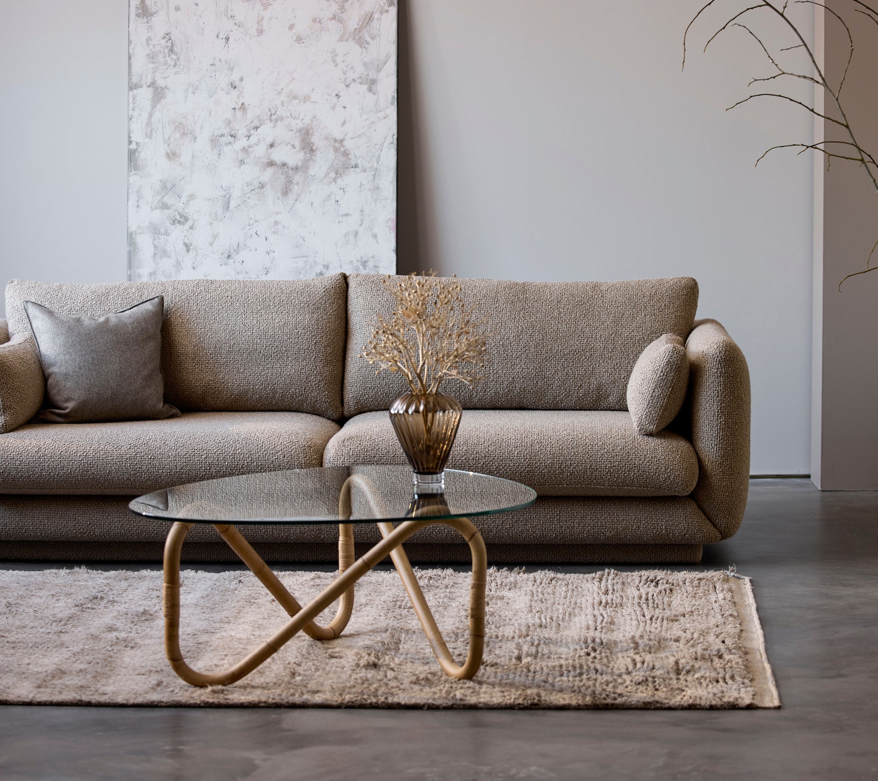 En moderne beige sofa med et glas sofabord og en dekorativ vase i en minimalistisk loungestil.