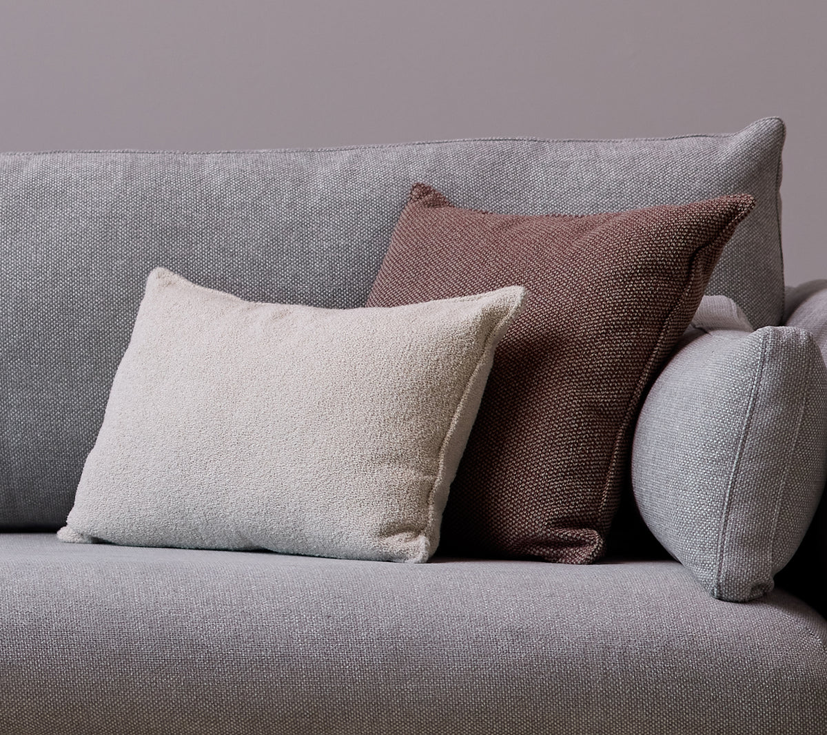 En hvid Scent scatterpude og en Wove mørkerød pude er placeret på en grå sofa.