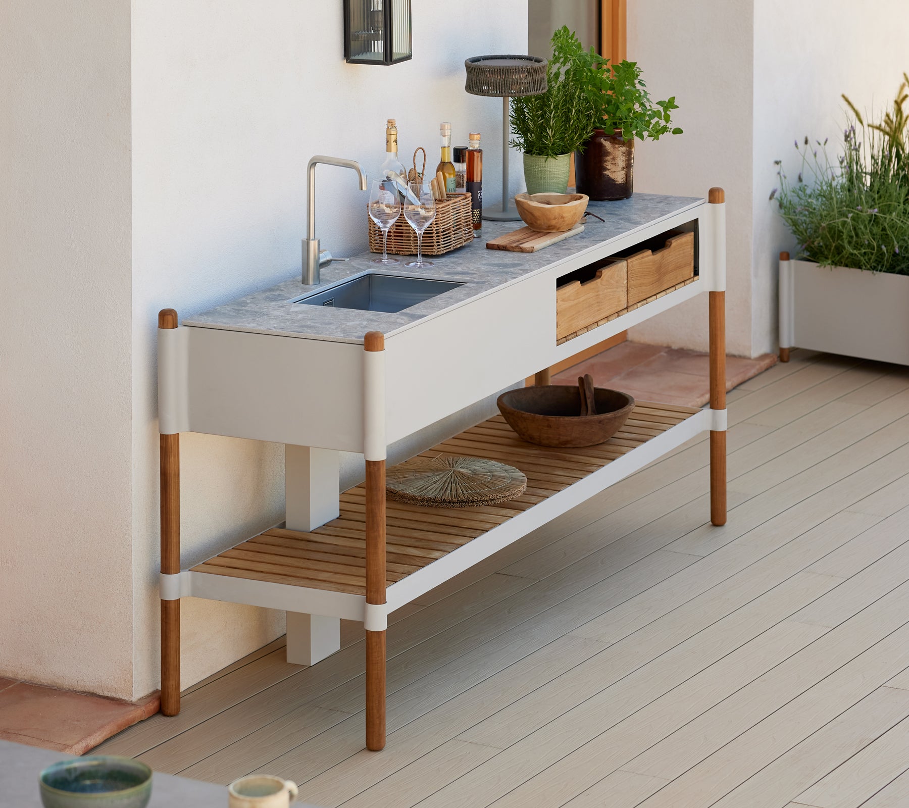 Et moderne, minimalistisk udendørs vaskestation med en granitbordplade, træopbevaringsskuffer og dekorative plantearrangementer.